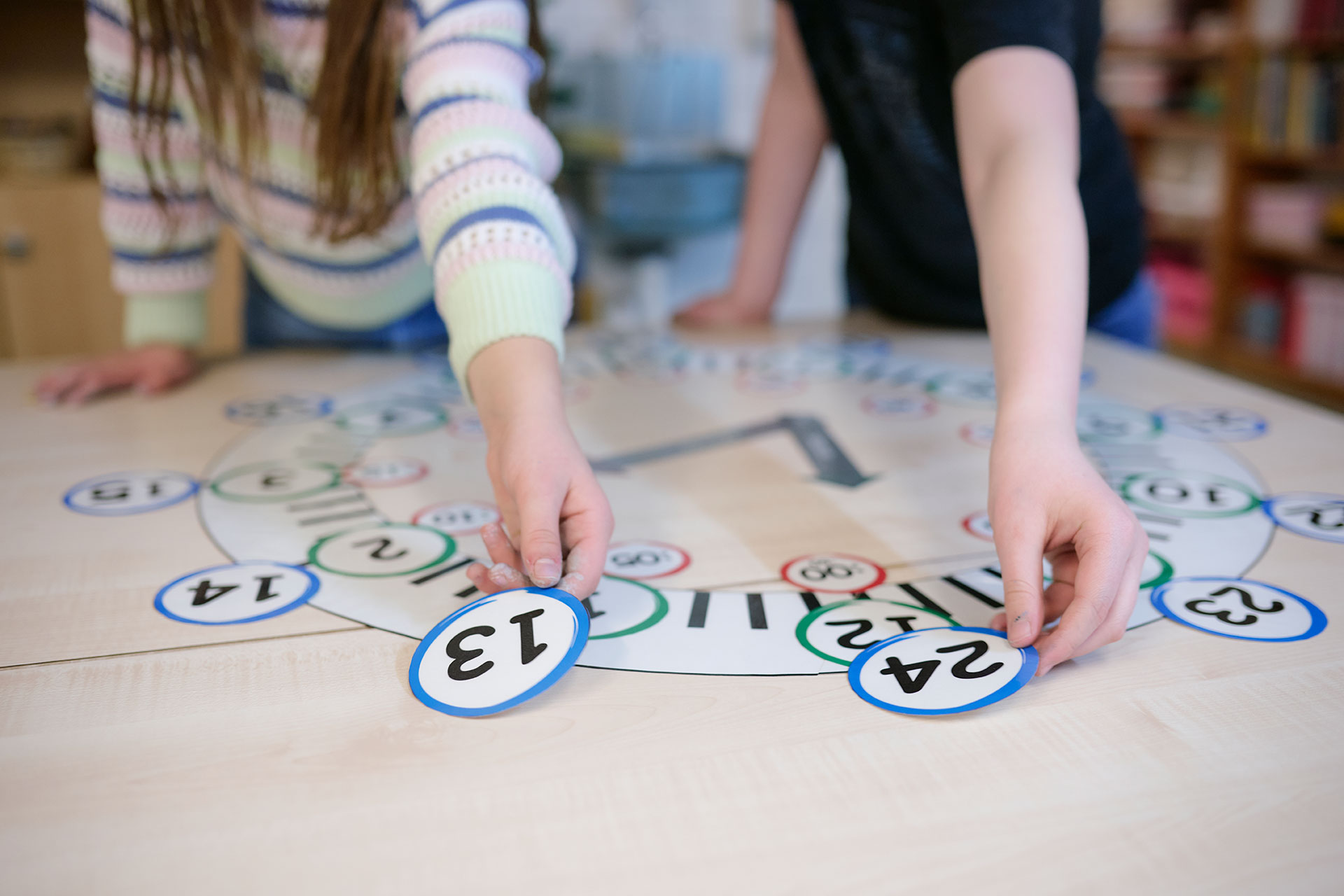 Kinder legen auf einer gebastelten Uhr verschiedene Uhrzeiten aus.