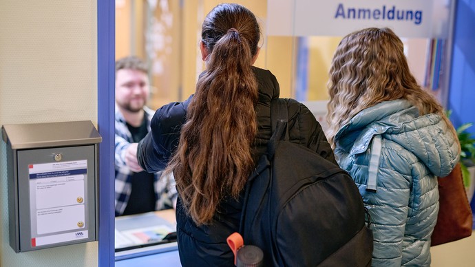 Eine Mutter und ihre Tochter, nur von hinten zu sehen, stehen an der Anmeldung der Klinik